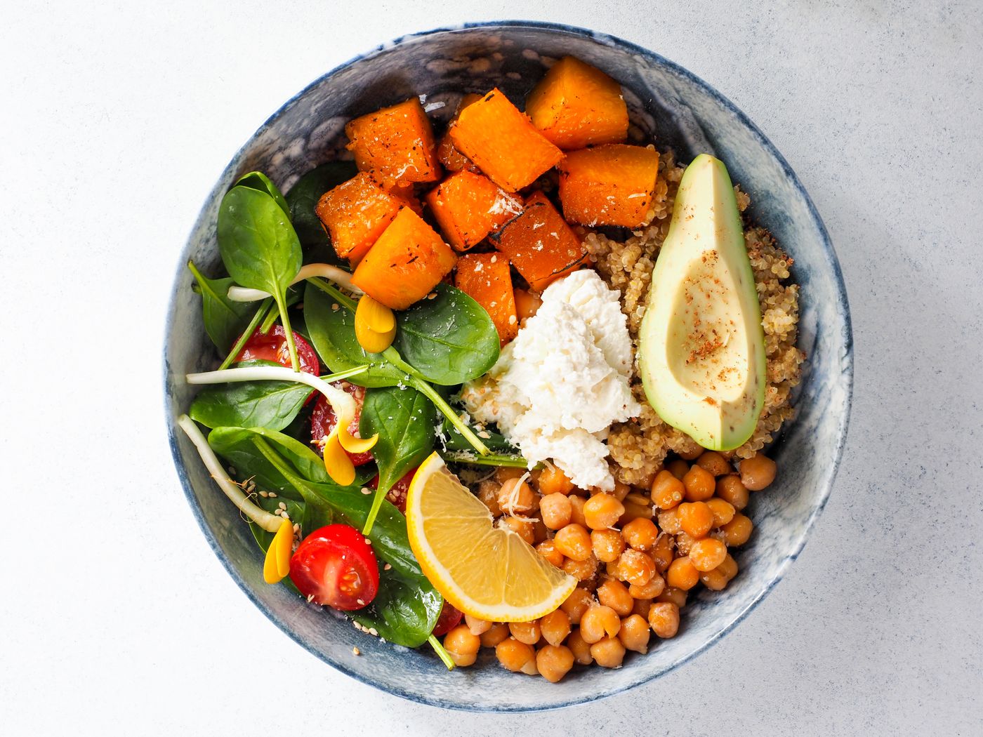 A plant-based bowl with avocado, chickpeas, sweet potato, spinach, lemon, and quinoa